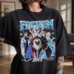 May include: Black t-shirt with the word "FROZEN" in a blue, icy font, and illustrations of characters from the animated film. The design includes Olaf, Anna, Elsa, Kristoff, and Sven.