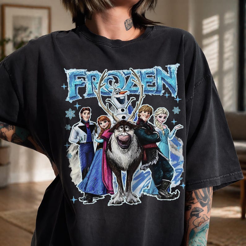May include: Black t-shirt with the word "FROZEN" in a blue, icy font, and illustrations of characters from the animated film. The design includes Olaf, Anna, Elsa, Kristoff, and Sven.