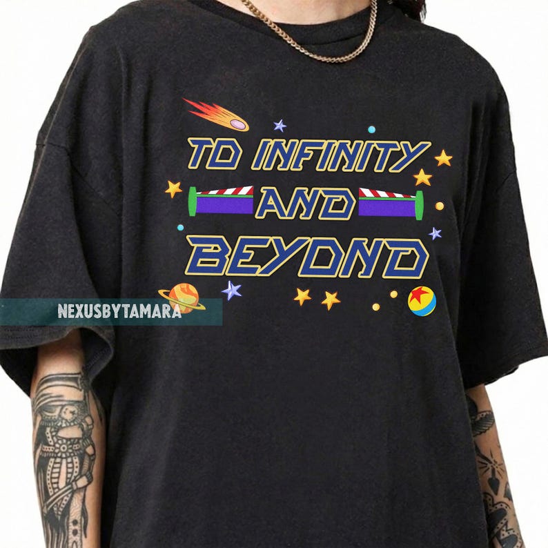 May include: Black t-shirt with the phrase "TO INFINITY AND BEYOND" in a colorful, cartoonish font. The design includes stars, a comet, and a planet. The shirt has a relaxed fit and short sleeves.
