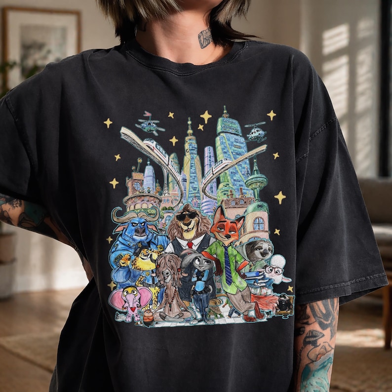 K&ouml;nnte beinhalten: Schwarzes T-Shirt mit einer farbenfrohen Illustration von Zootopia-Charakteren. Das Design zeigt Tierfiguren vor einer Stadtkulisse, komplett mit Sternen und einer Einschienenbahn. Das T-Shirt hat eine lockere Passform.