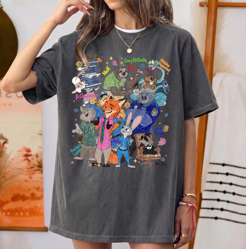 Op de afbeelding: Donkergrijs T-shirt met een kleurrijke illustratie van personages uit de film Zootopia. Het ontwerp bevat Judy Hopps, Nick Wilde en andere personages met hun namen. Het shirt heeft een ronde hals en korte mouwen.