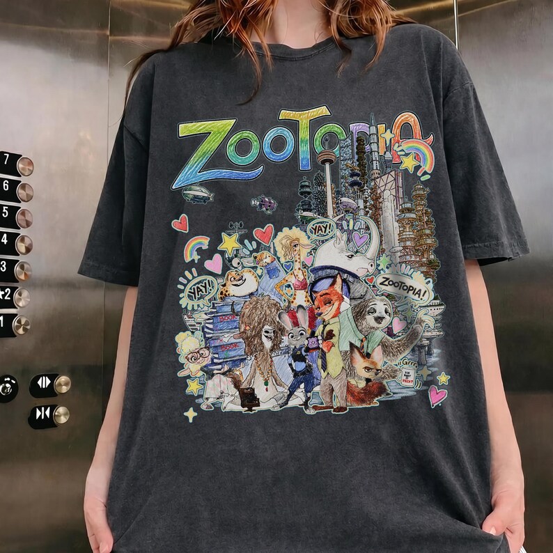 May include: Dark gray t-shirt featuring a colorful graphic from the animated film "Zootopia." The design includes the word "Zootopia" in rainbow colors, along with various characters and cityscapes. The shirt has short sleeves and a relaxed fit.