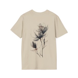 Könnte beinhalten: Beiges T-Shirt mit floralem Design auf dem Rücken. Das Design zeigt durchscheinende, dunkelgraue Magnolienblüten mit feinen Details. Das T-Shirt hat einen Rundhalsausschnitt und kurze Ärmel. Der Stil ist minimalistisch.
