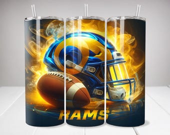 May include: A cylindrical tumbler with a clear straw featuring a graphic of a blue and yellow football helmet and a brown football surrounded by swirling orange and yellow flames. The word RAMS is printed in bold yellow letters at the bottom.