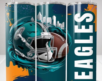 May include: A teal and dark blue stainless steel tumbler with a clear straw, featuring a teal football helmet, a brown football, a white city skyline silhouette, orange paint splatters, and the word EAGLES in large white vertical capital letters.