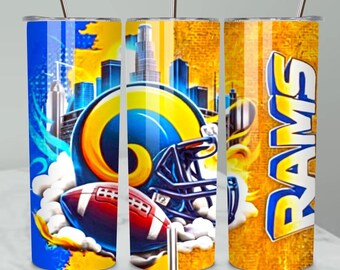 May include: A cylindrical tumbler with a straw featuring a blue and yellow graphic design of a football helmet, a football, and a city skyline. The word RAMS is printed vertically in large yellow letters with a blue outline on a textured gold background.
