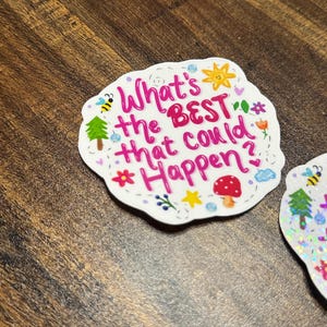 May include: A die-cut sticker with a scalloped edge featuring the pink text What's the BEST that could Happen? surrounded by small colourful illustrations including a yellow sun, a red mushroom, a green tree, a bee, flowers, and stars.