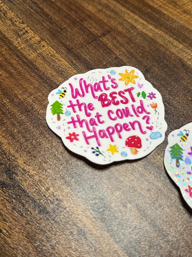 May include: A die-cut sticker with a scalloped edge featuring the pink text What's the BEST that could Happen? surrounded by small colourful illustrations including a yellow sun, a red mushroom, a green tree, a bee, flowers, and stars.