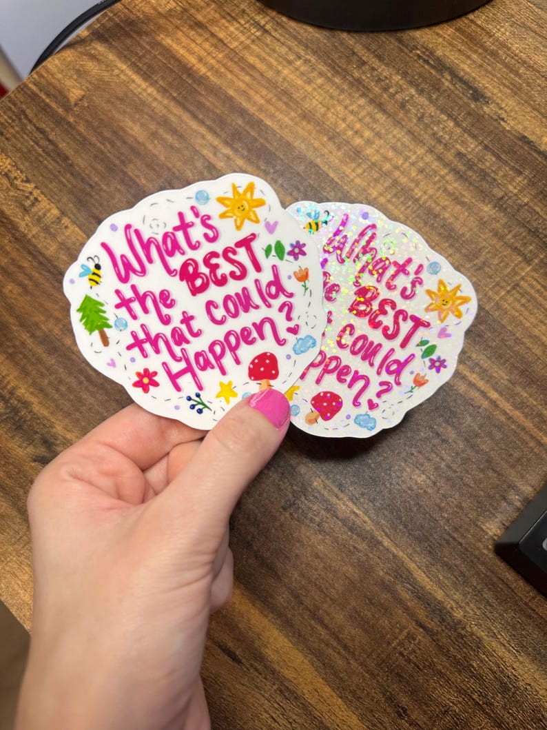 May include: Two die-cut holographic stickers featuring the pink text What's the BEST that could Happen? surrounded by colourful illustrations of a yellow sun, a red mushroom, a green tree, a bee, flowers, and blue clouds on a white background.