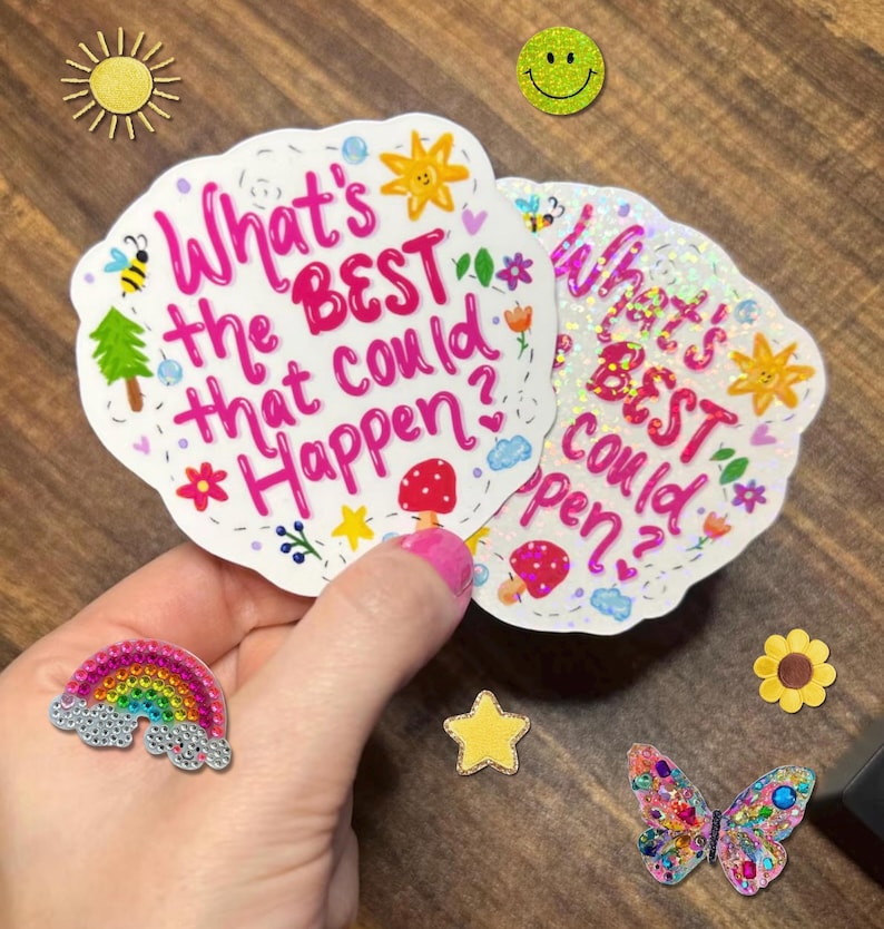 May include: Two die-cut stickers featuring the pink text What's the BEST that could happen? surrounded by small illustrations of a sun, bee, tree, mushroom, and flowers. One sticker has a holographic finish, while the other has a matte white finish.