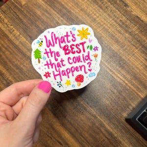 May include: A white die-cut sticker featuring the pink hand-lettered text What's the BEST that could Happen? surrounded by colourful illustrations of a yellow sun, a green tree, a red mushroom, a bee, flowers, stars, and small blue clouds.