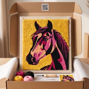 Op de afbeelding: Een punch needle knutselpakket in een kartonnen doos met een vierkant canvas met een paardenhoofdontwerp in geel, zwart en roze garen, vier kleine bolletjes garen, een houten punch needle tool, een metalen naaldinrijger en een bedrukte patroonkaart.