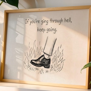 May include: Framed art print with a light wood frame. The artwork features a black and white illustration of a shoe stepping through flames, with the text "If you're going through hell, keep going."