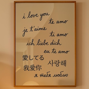 Peut inclure: Un cadre en bois affiche "Je t'aime" dans plusieurs langues sur un mur. Une lampe sphérique illumine un meuble en bois, encadré de plantes en pot. L'impression présente du texte noir sur un fond clair.