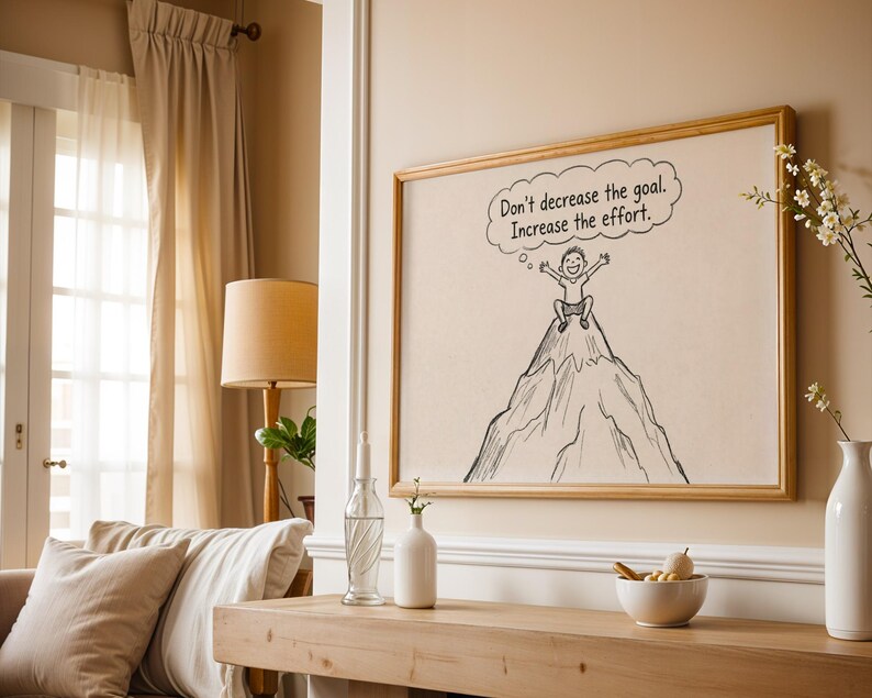 May include: A framed artwork with a motivational message. The artwork features a hand-drawn illustration of a person on a mountain peak with the text "Don't decrease the goal. Increase the effort." The frame is made of wood.