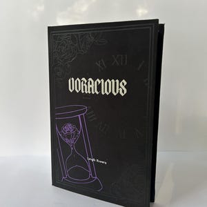 May include: A black book with the word "VORACIOUS" in white lettering. The cover features a purple hourglass design with a rose inside, and the author's name, Leigh Rivers. Floral and clock elements are also present.