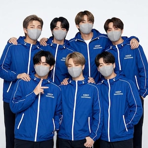 May include: Seven people wearing blue hooded jackets with white trim and the text "KEEP SWIMMING". Each person is wearing a gray face mask. The group is posing for a photo.
