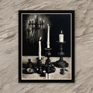 May include: A black and white framed print featuring lit candles in ornate holders, a small bottle, and a chandelier in the background. The print has a gothic or vintage aesthetic, with a dark and moody atmosphere.