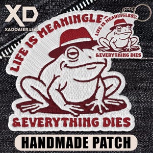 May include: Embroidered patch featuring a frog wearing a fedora, with the text "LIFE IS MEANINGLESS & EVERYTHING DIES." A smaller frog illustration is also present. The patch is white with burgundy details and the words "HANDMADE PATCH" at the bottom.
