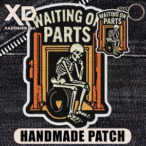 May include: Embroidered patch with a skeleton seated on a tire, inside a garage lift frame, with the text "WAITING ON PARTS." A smaller keychain version is also visible. The patch is labeled "HANDMADE PATCH."