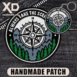 May include: Embroidered patch and keyring set with a compass design and the text "ALWAYS TAKE THE SCENIC ROUTE." The patch and keyring have a black border, a white background, and green trees. The patch also has the text "ALWAYS TAKE THE SCENIC" and "HANDMADE PATCH."