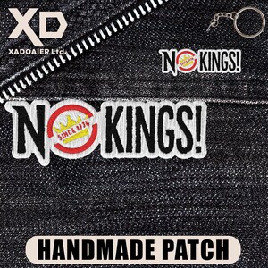 May include: Embroidered patches with the text "NO KINGS!" in white, black, and red. One patch includes a gold crown and the text "SINCE 1776". The patches are on a dark denim background with a zipper and a keychain.