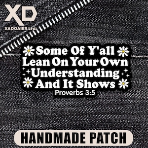 May include: A black and white handmade patch featuring the quote "Some Of Y'all Lean On Your Own Understanding And It Shows Proverbs 3:5" in a playful font, with flower and star embellishments. The patch is displayed on a dark denim fabric.
