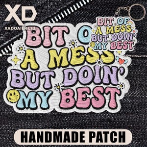 May include: Embroidered patch with the text "BIT OF A MESS BUT DOIN' MY BEST" in pastel colors. The patch includes a keychain and the words "HANDMADE PATCH" at the bottom. The background is a dark denim fabric.
