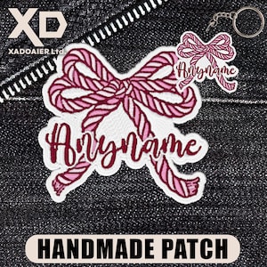May include: Embroidered patch and keychain featuring a pink and white bow design with the text "Anyname". The patch and keychain are on a dark denim background. The patch has the words "HANDMADE PATCH" at the bottom.