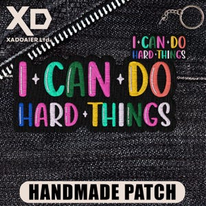 May include: Black embroidered patch with the text "I CAN DO HARD THINGS" in colorful letters. The patch also has the text "HANDMADE PATCH" at the bottom. The patch is on a dark denim background.