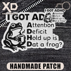 May include: Embroidered patch and keychain set with a frog holding a mug. The patch reads "I GOT ADHD" and "Attention Deficit Hold up is Dat a frog?" in black and white. The keychain has the same design.