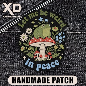 May include: Embroidered patch with a frog sitting on a mushroom, surrounded by flowers. Text reads "Let me be weird in peace." The patch is black with colorful details and the words "HANDMADE PATCH" at the bottom.