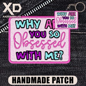 May include: A handmade patch with the text "WHY ARE YOU SO OBSESSED WITH ME?" in turquoise, purple, and pink. A smaller keychain version of the patch is also visible. The patch is on a denim background.