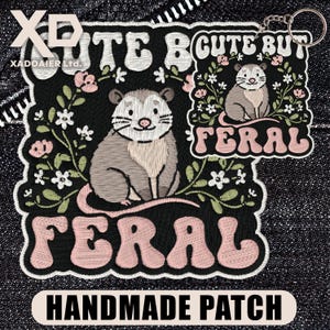 May include: Embroidered patch and keychain featuring a cute opossum design. The patch has the text "Cute But Feral" and "Handmade Patch". The opossum is gray and beige, surrounded by flowers on a black background.