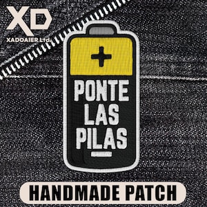 May include: Embroidered patch in the shape of a battery with a yellow top and a black body. The patch features the text "PONTE LAS PILAS" in white, with a plus sign symbol. The bottom of the patch reads "HANDMADE PATCH".