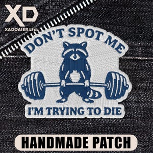 May include: Embroidered patch featuring a blue raccoon lifting a barbell, with the text "DON'T SPOT ME" above and "I'M TRYING TO DIE" below. The patch is labeled "HANDMADE PATCH".