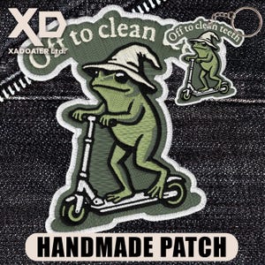 May include: A handmade patch featuring a green frog riding a scooter and wearing a witch hat. The patch has the text "Off to clean" and "Handmade Patch". A keychain with a similar design is also visible.