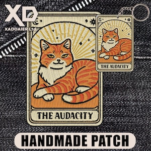 May include: Embroidered patch and keychain featuring a ginger cat in a tarot card design. The patch and keychain have the text "THE AUDACITY" at the bottom. The patch is rectangular, and the keychain is smaller with a silver keyring.