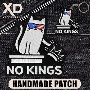May include: Embroidered patches and a keychain featuring a white cat wearing sunglasses with a red, white, and blue design. The patches and keychain have the text "NO KINGS" and "HANDMADE PATCH".