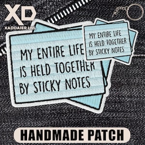 May include: A handmade patch with the text "MY ENTIRE LIFE IS HELD TOGETHER BY STICKY NOTES" in black on a light blue background. The patch has a white border and is on a dark denim background. A keychain is visible.