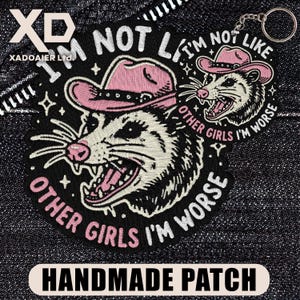 May include: Embroidered black patch featuring a possum wearing a pink cowboy hat, with the text "I'M NOT LIKE OTHER GIRLS I'M WORSE." The patch also includes the words "HANDMADE PATCH."
