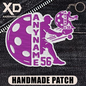 May include: A handmade purple patch with white stitching featuring a pickleball design. The patch includes the text "ANYNAME 56" and a pickleball player silhouette. The words "HANDMADE PATCH" are printed at the bottom.