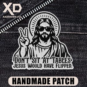 May include: Embroidered patch featuring a stylized image of Jesus wearing sunglasses and making a peace sign. The patch includes the text "DON'T SIT AT TABLES JESUS WOULD HAVE FLIPPED" and "HANDMADE PATCH".