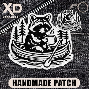 May include: A black and white patch and keychain set featuring a raccoon in a canoe, holding a mug. The patch and keychain have a forest scene design. The patch has the text "HANDMADE PATCH". The brand name "XADOAIER Ltd." is also visible.