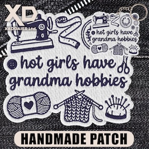 May include: Embroidered patch with the text "hot girls have grandma hobbies" and illustrations of sewing, knitting, and yarn. The patch is white with navy blue details and the words "HANDMADE PATCH" at the bottom.