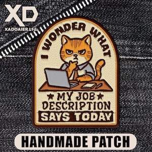 May include: Embroidered patch with a cartoon cat looking disgruntled at a desk with a laptop. Text says "I WONDER WHAT MY JOB DESCRIPTION SAYS TODAY." The patch has a brown border and the words "HANDMADE PATCH" at the bottom.