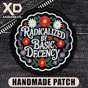 May include: A round, black embroidered patch with the text "RADICALIZED BY BASIC DECENCY" in white script. The patch is decorated with red poppies, white daisies, and purple lavender. The words "HANDMADE PATCH" are at the bottom.