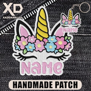 May include: Embroidered unicorn patch with a yellow horn, pink ears, and a floral crown of pink and blue flowers. The name "Name" is embroidered in pink. A matching keychain is also present. The patch reads "HANDMADE PATCH".