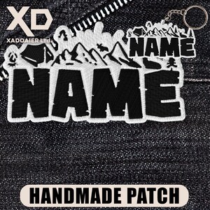 May include: Black and white embroidered patch with the word "NAME" in bold letters. The patch features a mountain and camping scene design. The text "HANDMADE PATCH" is at the bottom. A keychain with the same design is attached.
