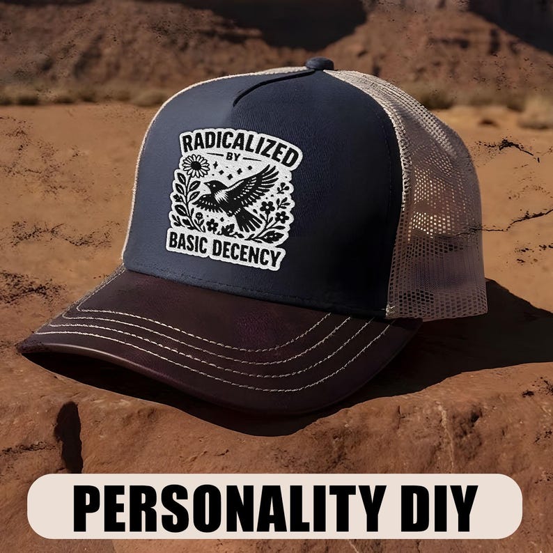 Peut inclure: Casquette de camionneur bleu marine et marron avec un dos en filet beige. L'avant du chapeau pr&eacute;sente un carr&eacute; blanc avec les mots "RADICALIZED BY BASIC DECENCY" entourant un graphique d'oiseau noir. La visi&egrave;re est marron.